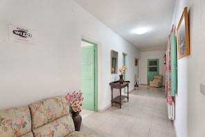 A hallway with a sofa, a table with a vase, and a chair.