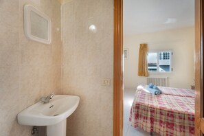 A bathroom with a sink and a mirror, a bedroom with a bed and a window, and a view of a building outside.