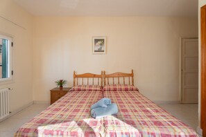 A bedroom with a bed, a nightstand, a potted plant, and a framed picture on the wall.
