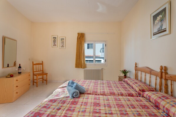 A bedroom with a bed, a wooden dresser, a chair, a window with a curtain, and a radiator.