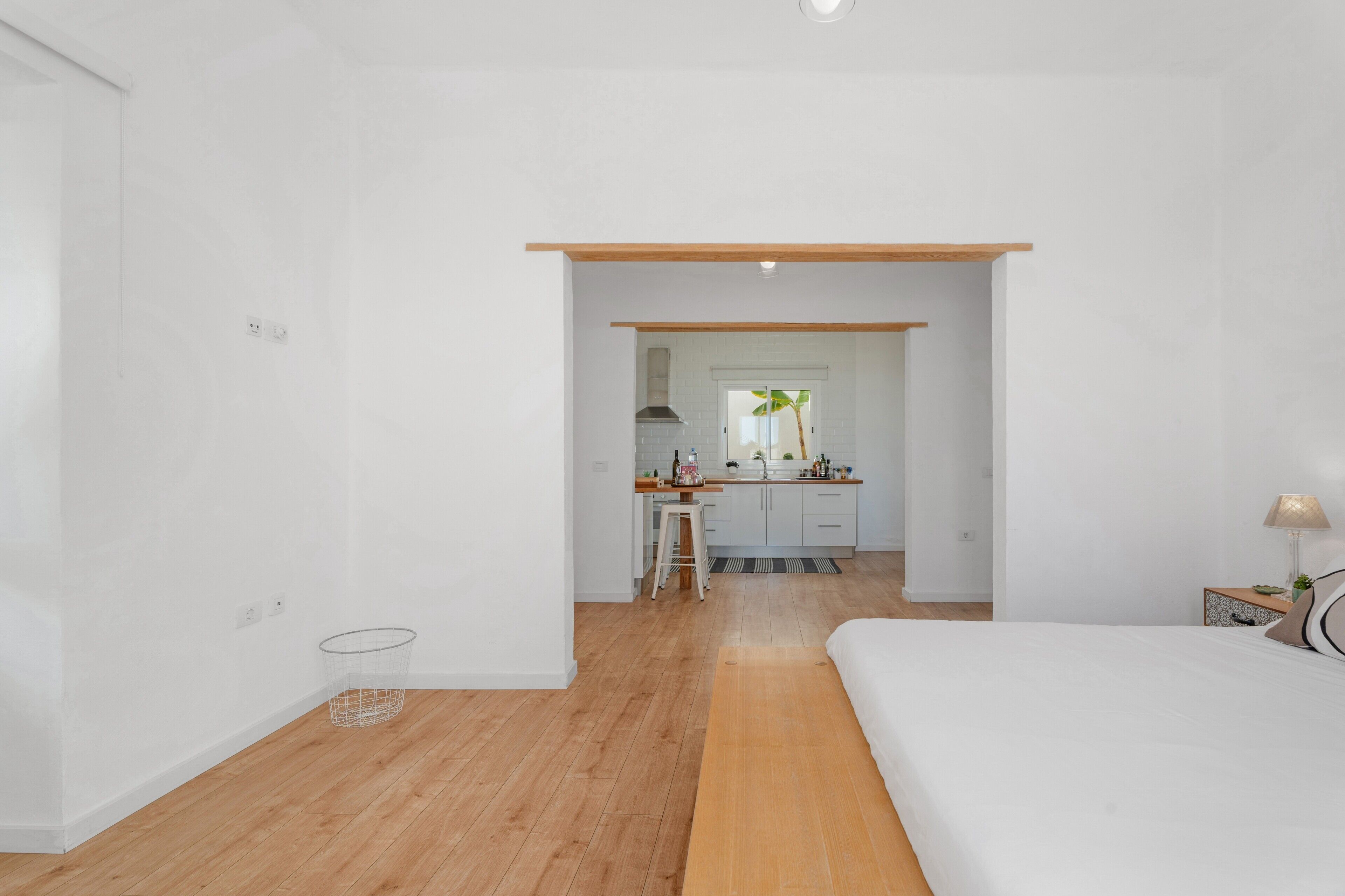 Een moderne hotelkamer met een houten vloer, een bed, een bureau en een kitchenette op de achtergrond.