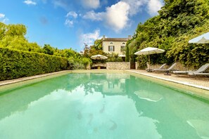 A swimming pool with lounge chairs and umbrellas, surrounded by greenery and a stone wall. - Chez Jacquou – Authentic Charm and Modern Comfort with Private Pool in the Heart of Périgord (Bouniagues)