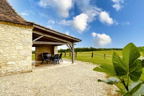 A stone building with a covered patio, outdoor seating, and a view of a green field. - Chez Jacquou – Authentic Charm and Modern Comfort with Private Pool in the Heart of Périgord (Bouniagues)