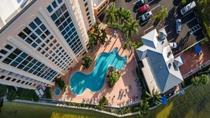 Vue aérienne d’un hôtel doté d’une piscine, entouré de palmiers et de chaises longues.
