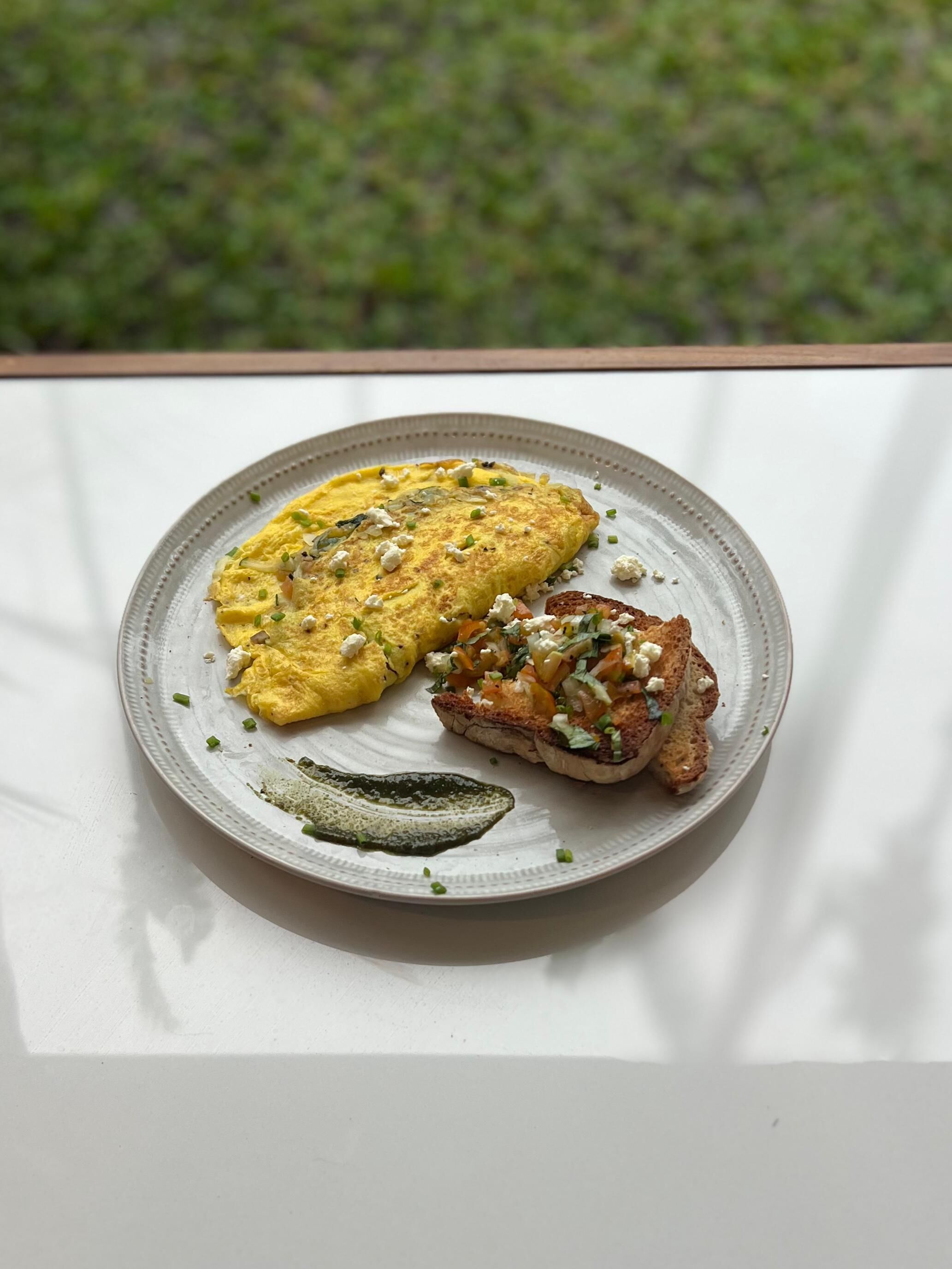 Un plato con tortilla, verduras a la parrilla y una rebanada de pan sobre una mesa blanca.