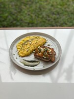 Un plato con tortilla, verduras a la parrilla y una rebanada de pan sobre una mesa blanca.