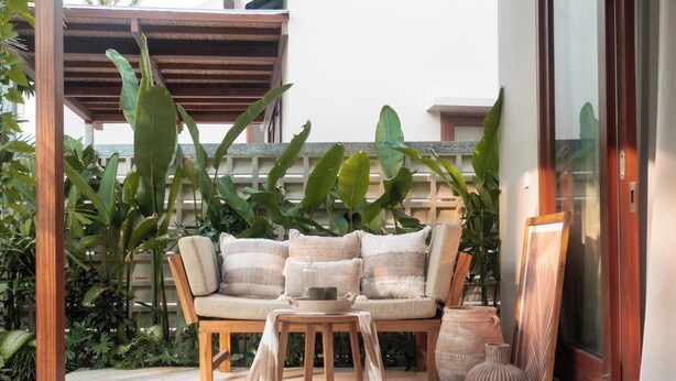 Une chaise en bois avec des coussins, une petite table et un vase.