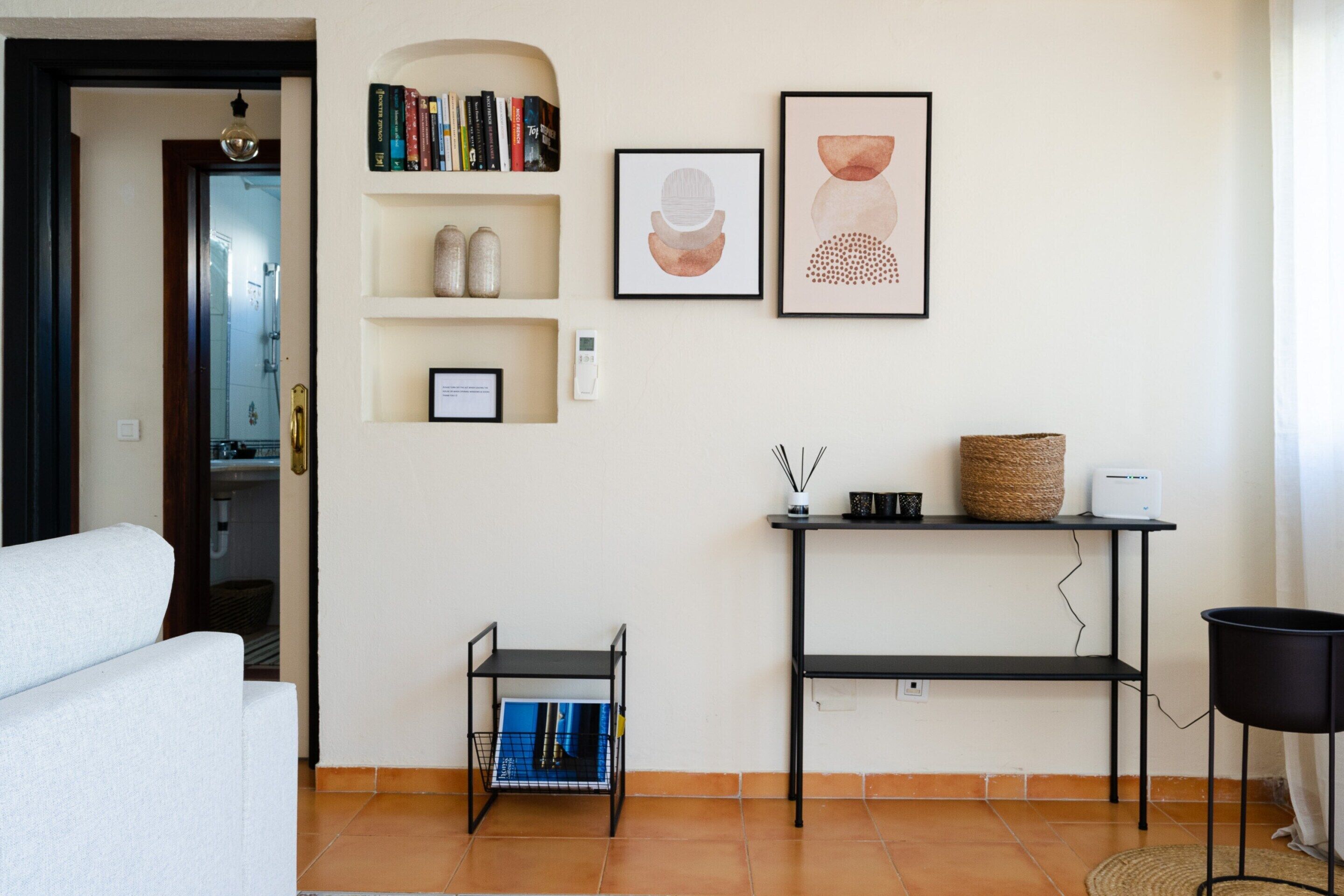 A modern living room with a sofa, a small black table with a basket, and a shelf with books and decorative items.