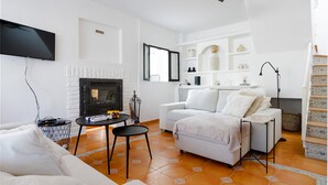 Una sala de estar moderna con chimenea, sofás blancos, un televisor y un ventilador de techo.