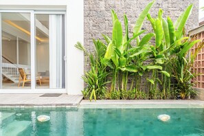 A swimming pool with a stone wall and tropical plants. - Villa Rasa Cinta  (Canggu)