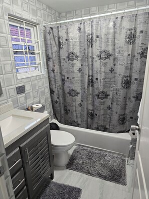 A bathroom with a toilet, bathtub, and a window with a grid pattern. - Soleil Paradise Palms  (St. Ann's Bay)
