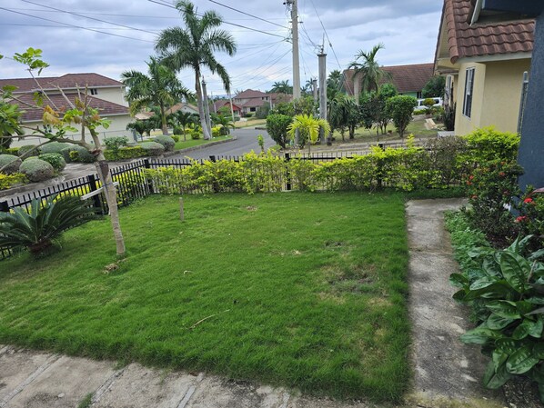 A residential area with a well-maintained lawn, a black metal fence, and houses with red-tiled roofs. - Soleil Paradise Palms  (St. Ann's Bay)