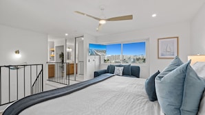 A modern bedroom with a large bed, a ceiling fan, and a city view through a window.