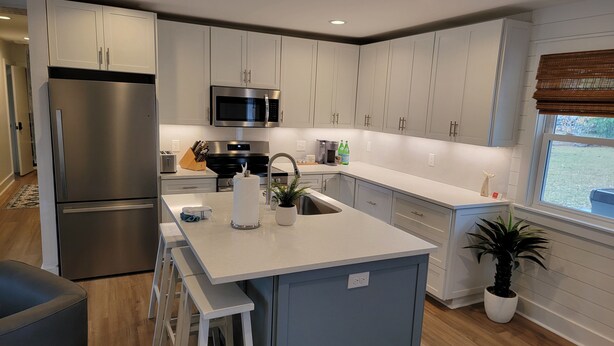 Una cocina moderna con electrodomésticos de acero inoxidable, armarios blancos y una isla central con taburetes.
