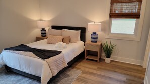 Un dormitorio ordenado con cama, mesitas de noche, una ventana con persianas y una planta en maceta.