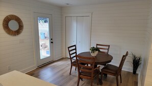 Un comedor con una mesa redonda de madera, cuatro sillas, una planta en maceta y una puerta que da al exterior.