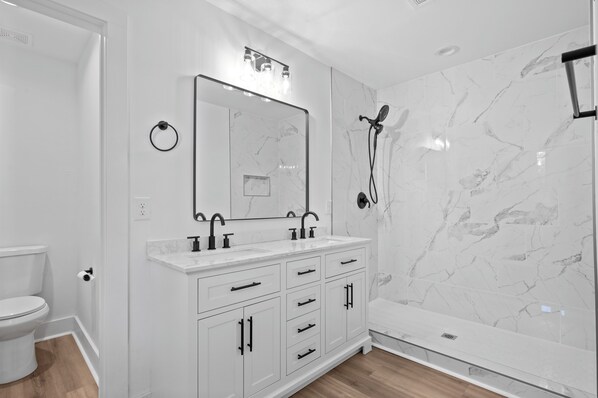 Een moderne badkamer met een witte wastafel, een grote spiegel en een douche met een marmeren wand.
