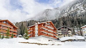 A snow-covered mountain resort with multi-story buildings featuring balconies and a ski lift visible in the background. - Edelweiss B by Interhome (Leukerbad)