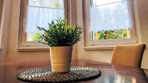A dining table with a potted plant, two arched windows with curtains, and a chair. - Edelweiss B by Interhome (Leukerbad)
