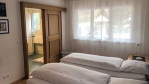 A bedroom with two beds, a wooden wardrobe, a window with curtains, and a view of the outside. - Edelweiss B by Interhome (Leukerbad)