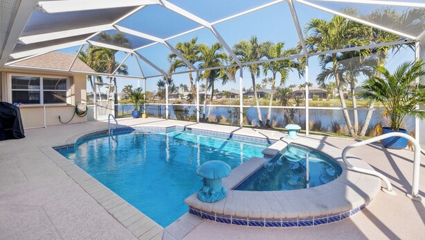 A pool area with a hot tub, surrounded by a covered deck and palm trees. - Lakefront view with Pool & Spa, large Patio, close to Beaches and Shopping! Monthly Discount (Fort Myers)