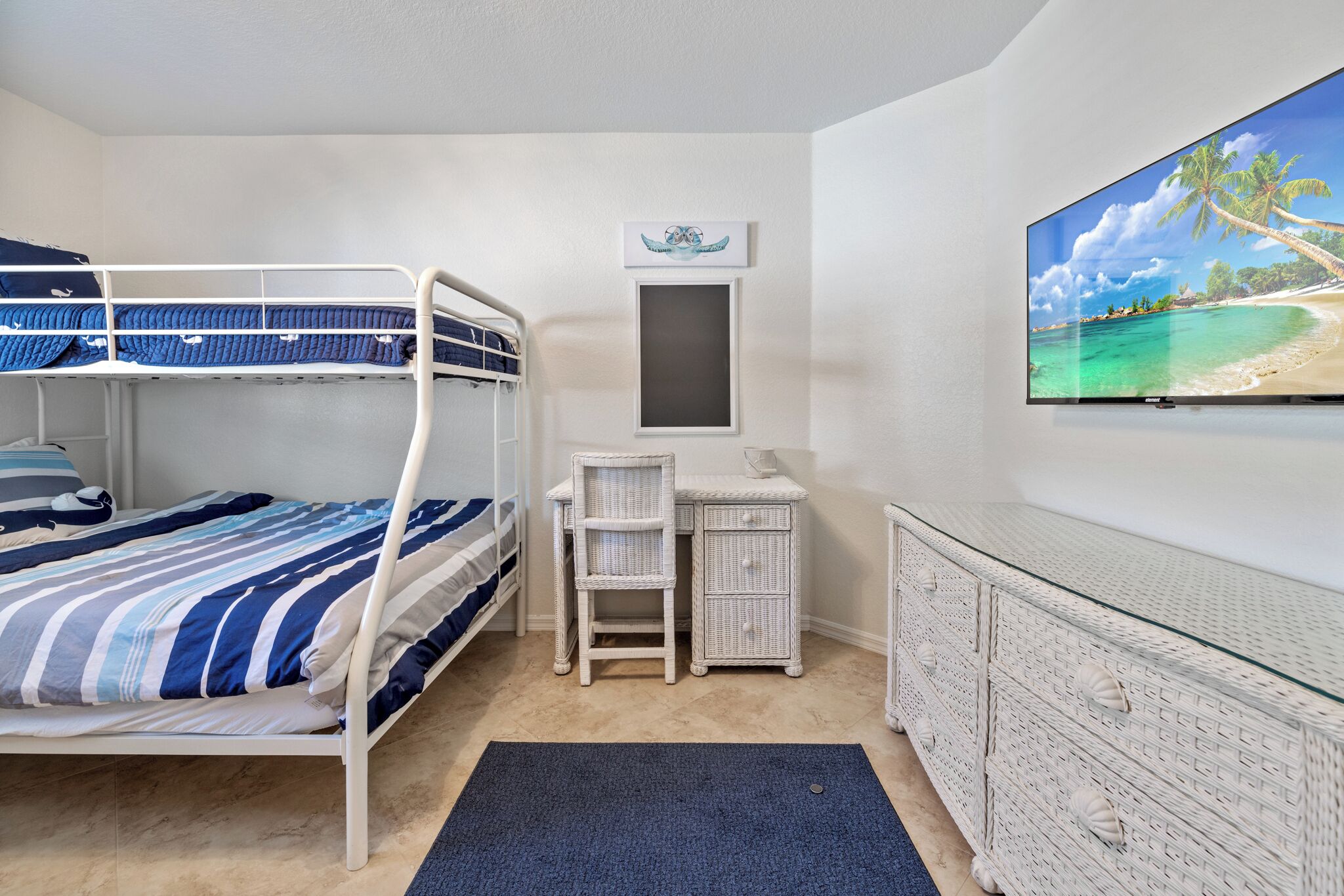 A bunk bed with striped bedding, a desk with a chair, a television, and a dresser.