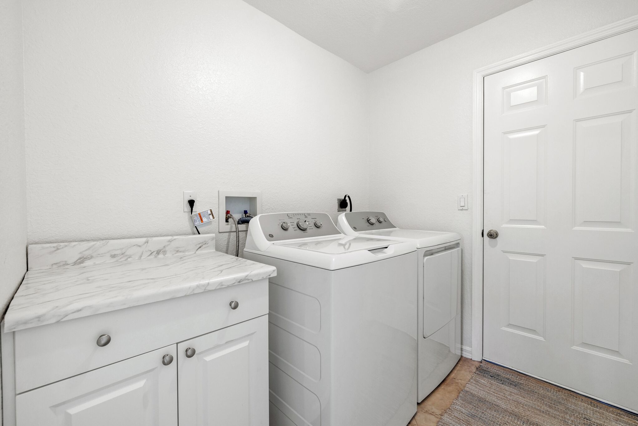 A laundry room with a white washing machine, dryer, and a marble countertop.