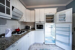 A kitchen with white cabinets, a microwave, an oven, and a refrigerator with multiple compartments. - Yamak Stone House (Urgup)