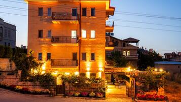 A multi-story building with balconies, a gated entrance, and a sign indicating 'Cappadocia Yamak Stone House.'