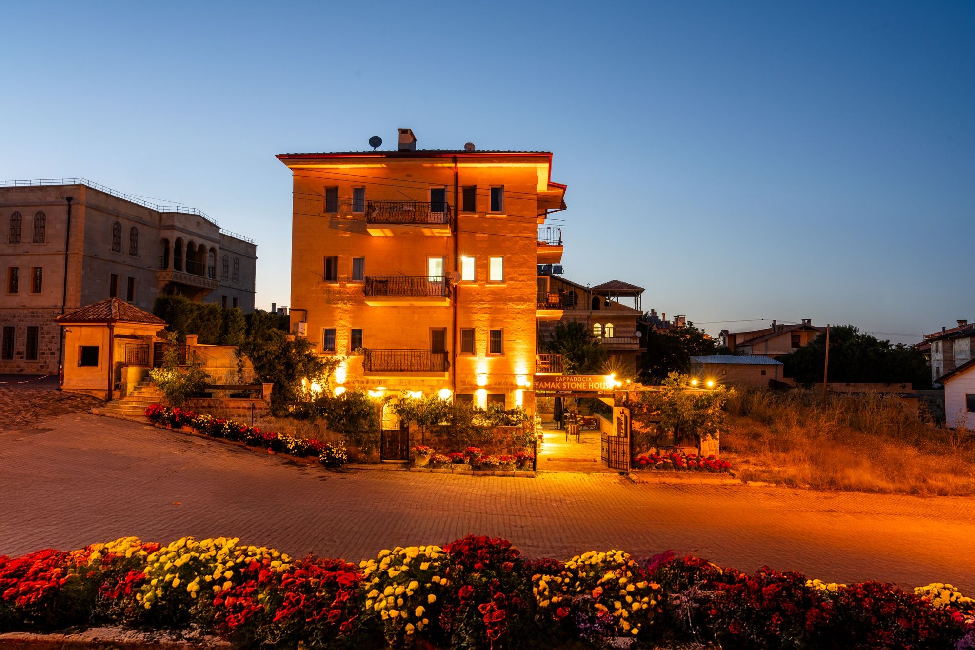 A multi-story building with balconies, a paved entrance, and a flower garden.