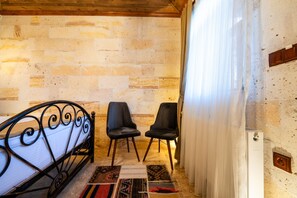 A room with a bed, two chairs, a patterned rug, and a curtain. - Yamak Stone House (Urgup)
