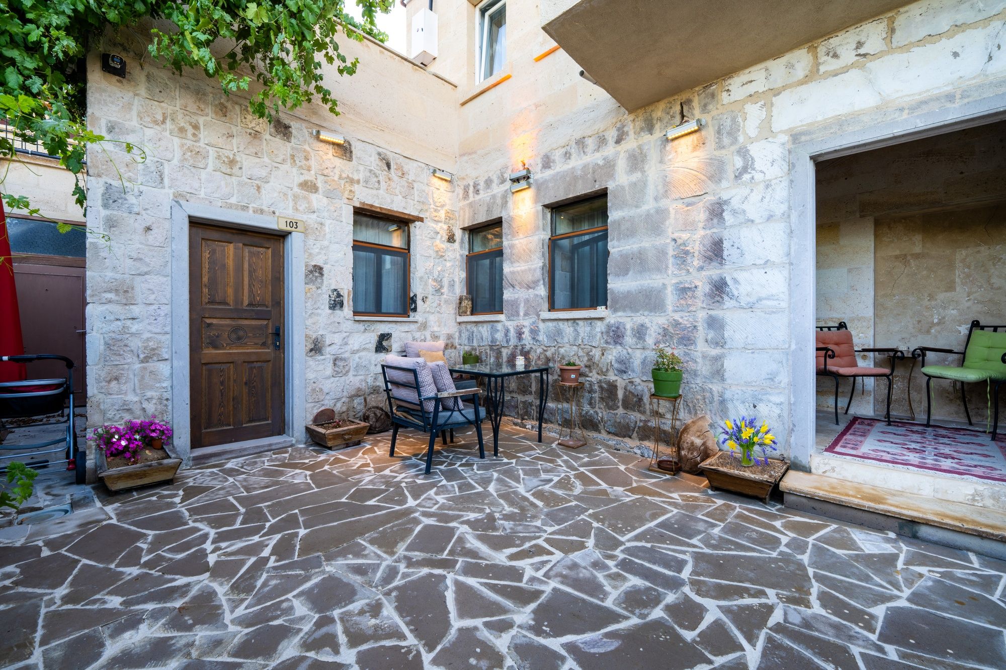 Un patio de piedra con una puerta de madera, una mesa con sillas y plantas en macetas.