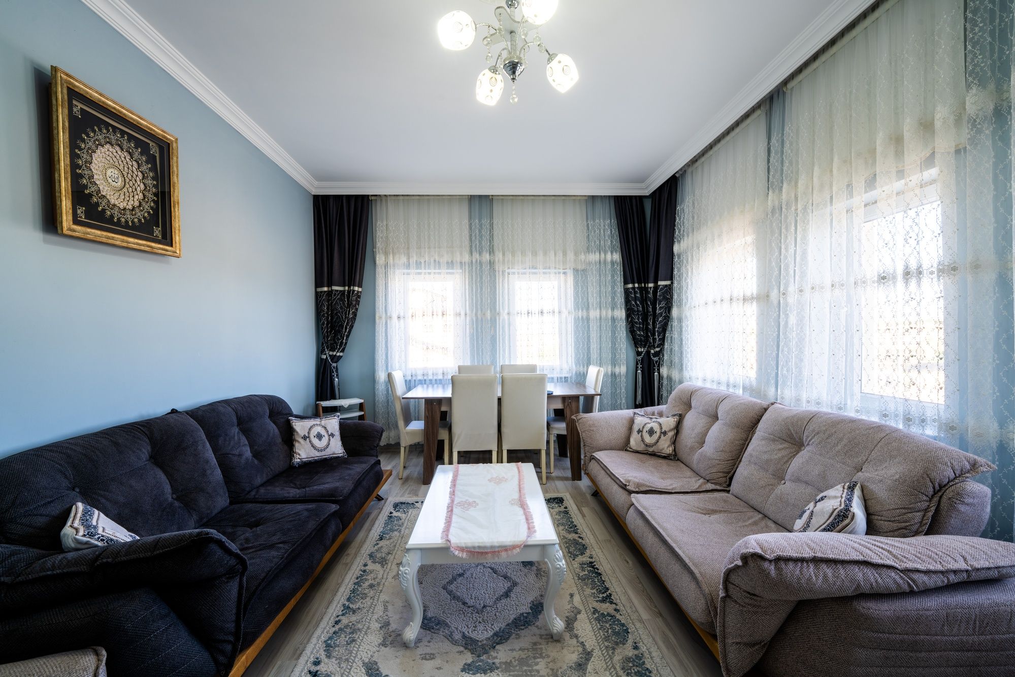 Una sala de estar con un sofá negro, un sofá color beige, una mesa de centro y un comedor con mesa y sillas.