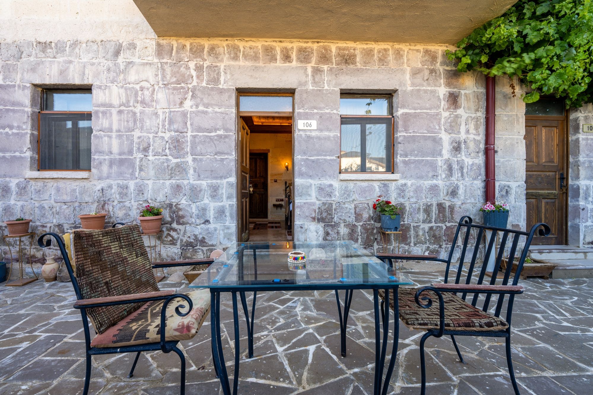 An outdoor seating area with a glass table and metal chairs, stone walls, and potted plants.