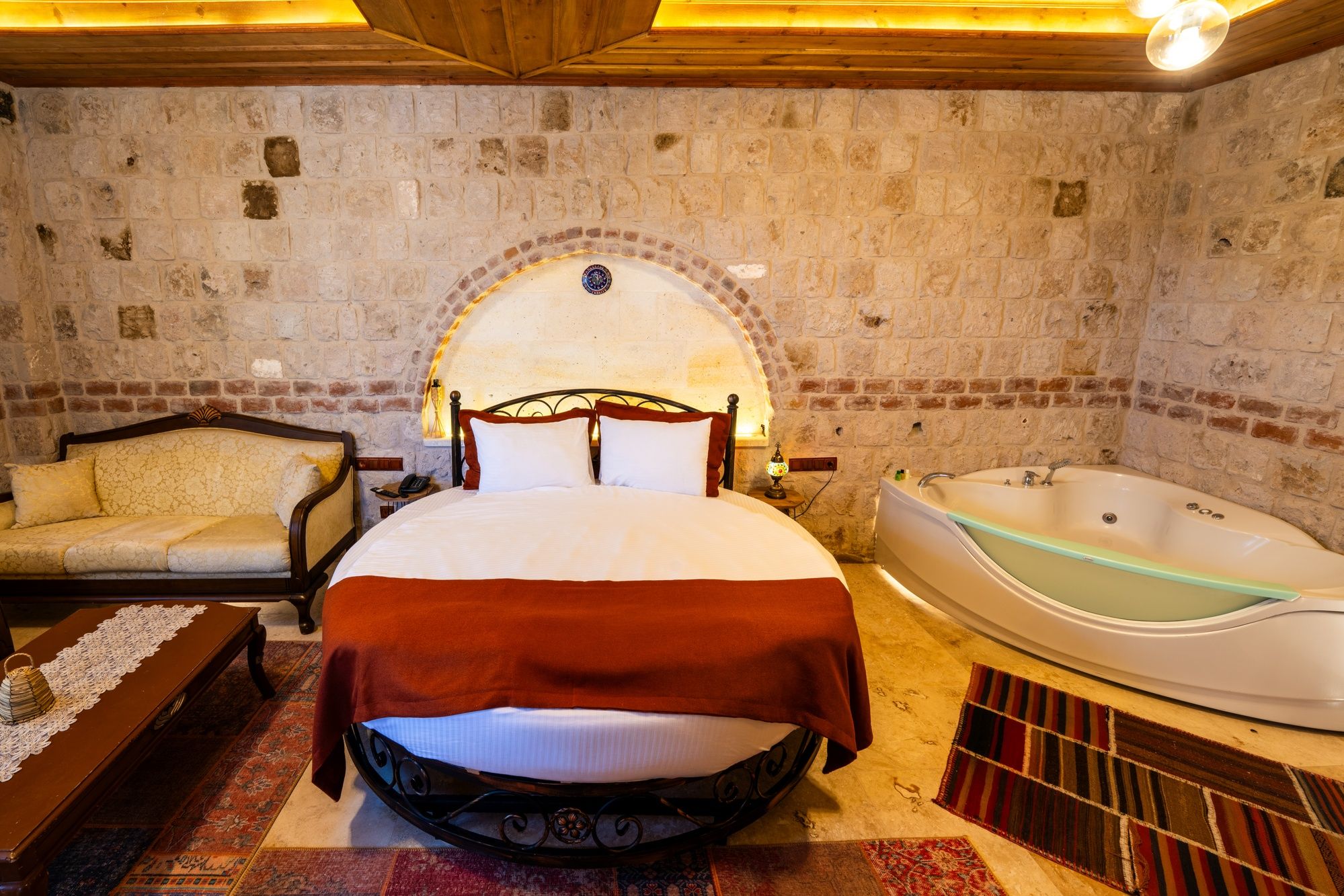 Un dormitorio con cama, sofá, bañera y pared de piedra.