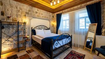 Un dormitorio con pared de piedra, cama con estructura de metal, techo de madera y una ventana grande con cortinas.