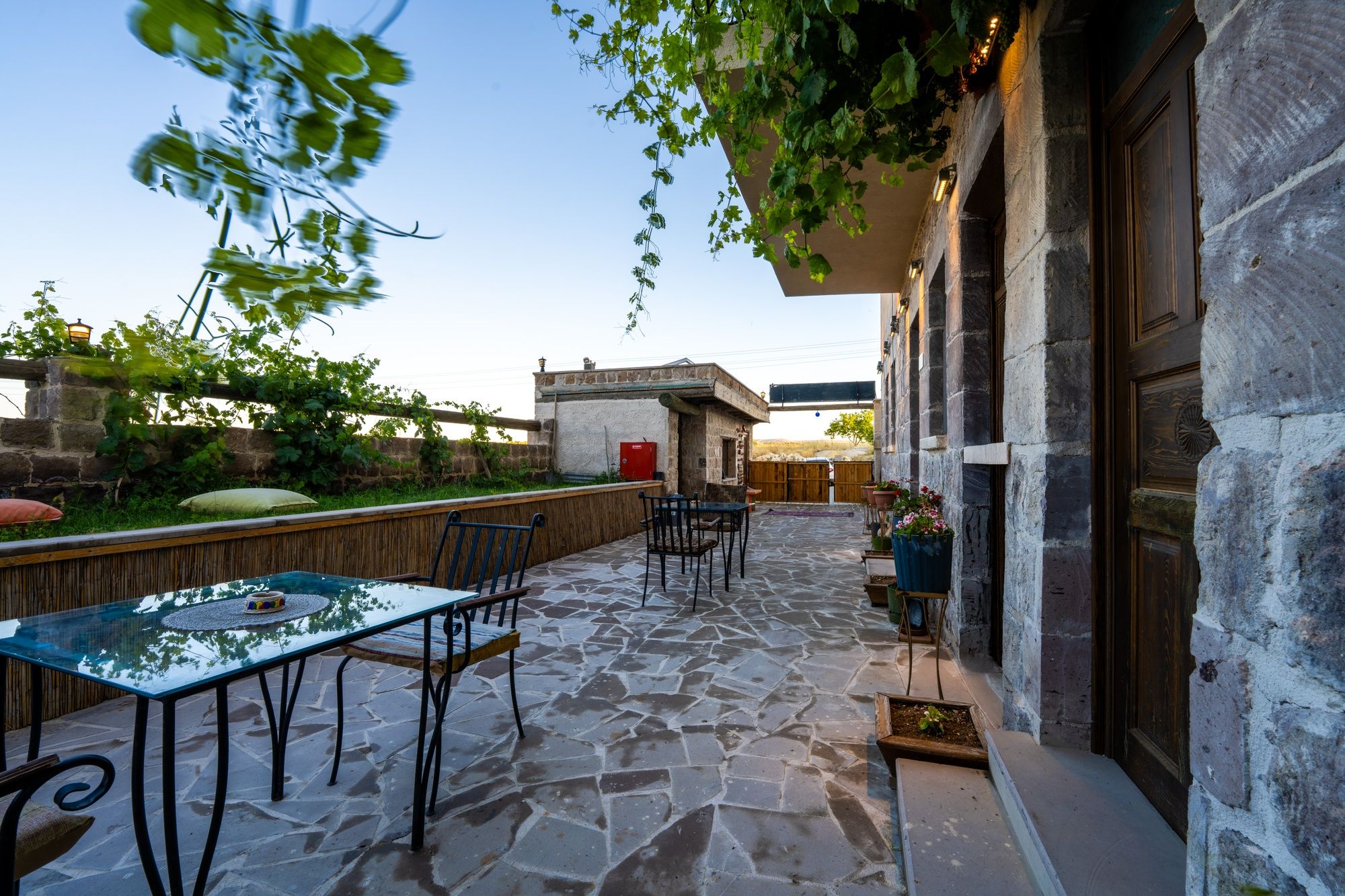 Un patio al aire libre con piso de piedra, una mesa de vidrio y sillas de metal.
