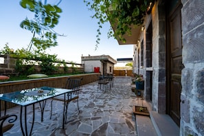 An outdoor patio with stone flooring, a glass table, and metal chairs. - Yamak Stone House (Urgup)