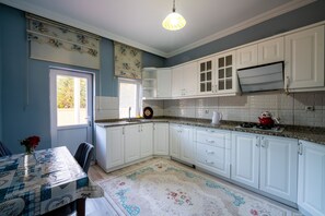 A kitchen with white cabinets, a granite countertop, a red teapot, and a patterned rug. - Yamak Stone House (Urgup)