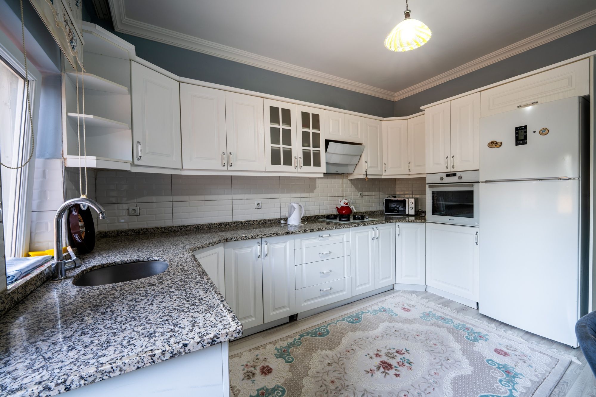 A kitchen with white cabinets, a granite countertop, a built-in oven, and a refrigerator.