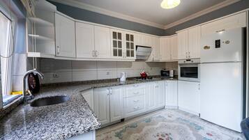 A kitchen with white cabinets, a granite countertop, a built-in oven, and a refrigerator.