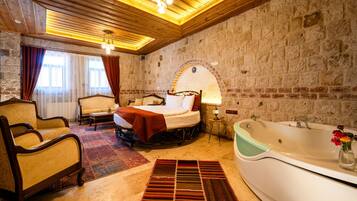 A hotel room with a bed, a sofa, a chair, a bathtub, and a stone wall.