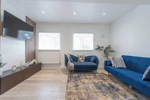 A modern living room with a blue sofa, a flat-screen TV, and a large window.