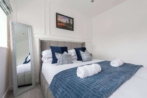 Un lit bien fait, avec une couette bleue, des oreillers blancs et un coussin à rayures.