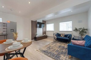 Ein modernes Wohnzimmer mit Essplatz, einer Couch und einer Küchenzeile mit Kühlschrank.