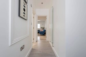 Un couloir avec une porte sur la gauche, une chaise bleue à l’arrière-plan et un interrupteur sur le mur.
