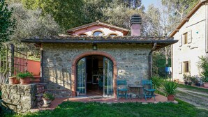 A stone building with a tiled roof, an arched entrance, and a small patio with chairs and potted plants. - Amazing apartment in Reggello with WiFi (Reggello)