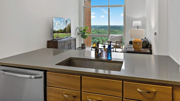 Een moderne keuken met een groot eiland, een inbouw vaatwasser, en uitzicht op een groen landschap door een groot raam.