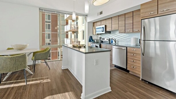 A modern kitchen with a central island, wooden cabinets, stainless steel appliances, and a dining area with a table and chairs.
