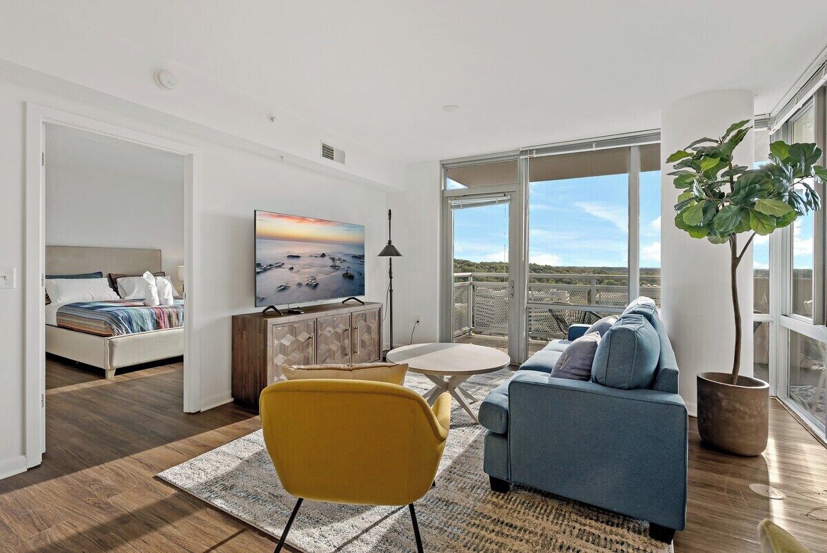 A modern living room with a sofa, a yellow chair, a TV, and a large window with a view.